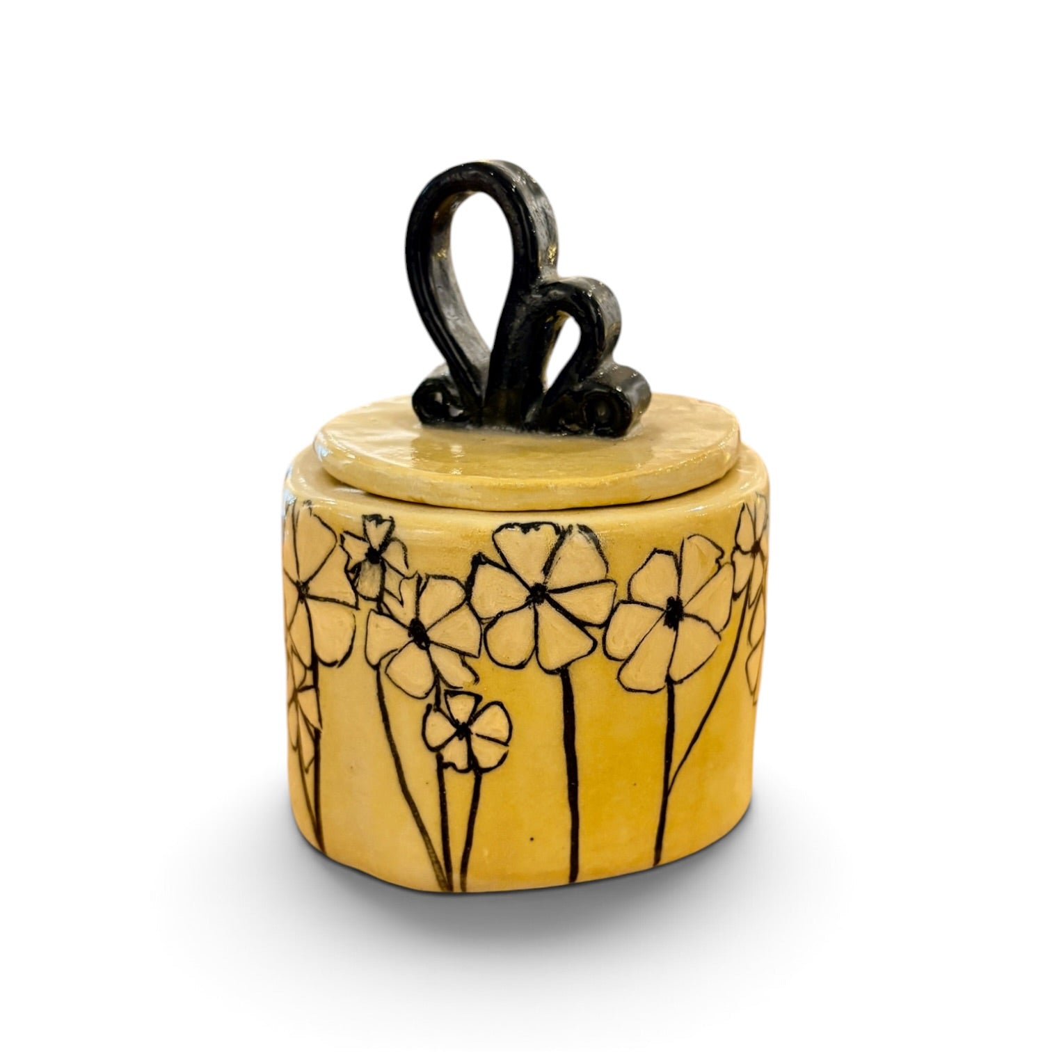 A small yellow ceramic lidded container with a black hand-painted floral pattern on the body and a black loop handle on top, shown on a white background.