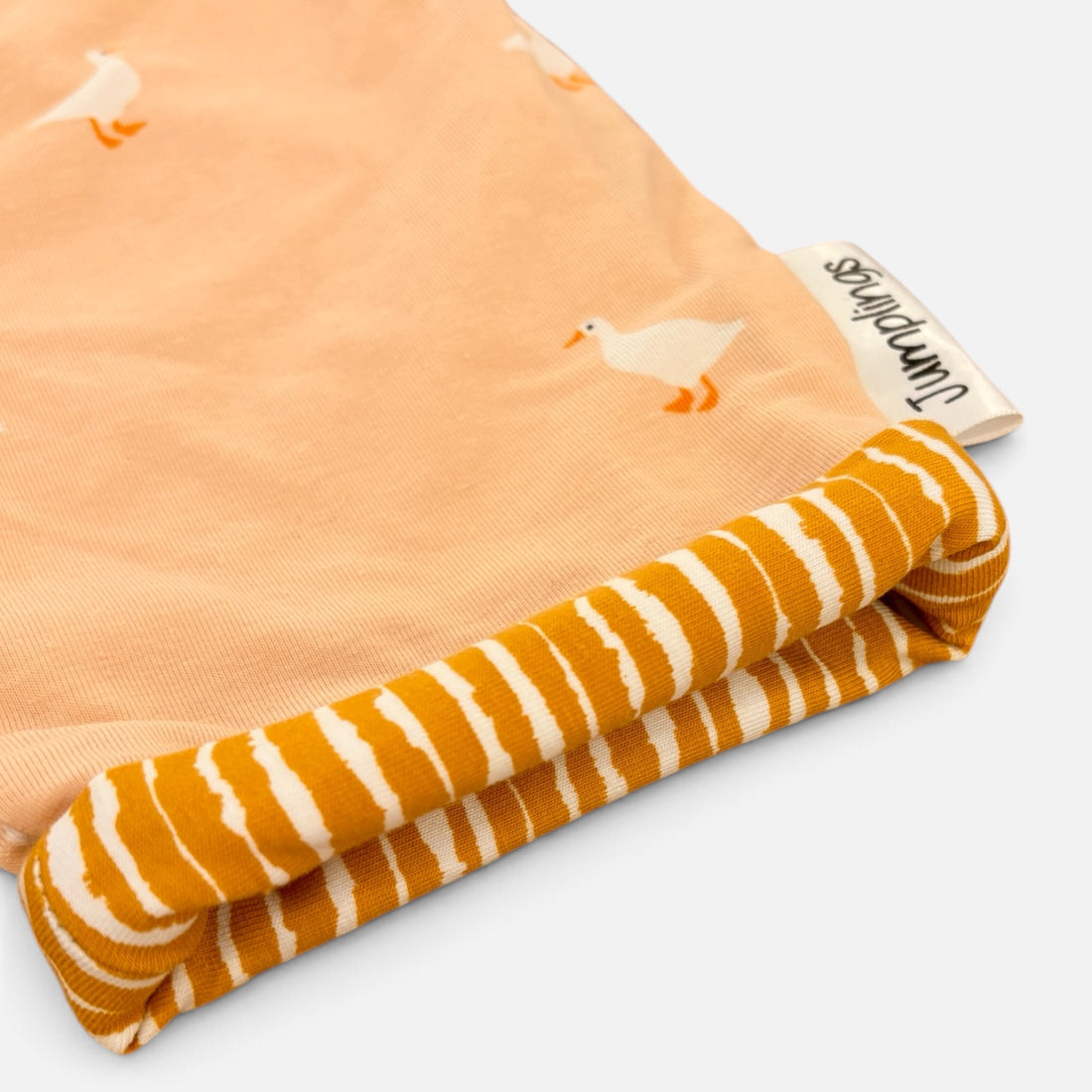 A folded baby blanket or fabric item on a light gray background. The top section is peach with a white duck print, and the folded bottom section shows a mustard yellow and white striped reverse side.