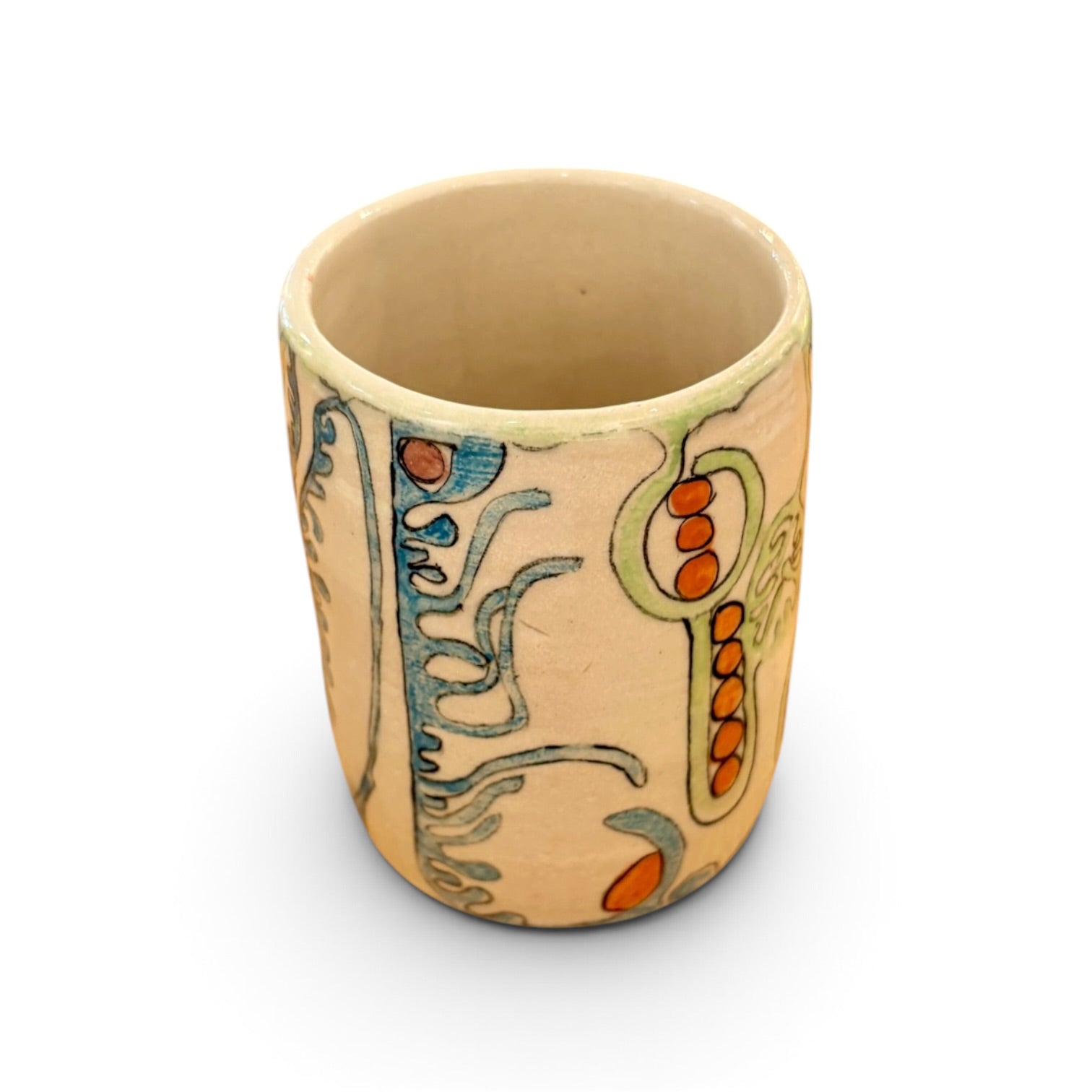 A handmade ceramic cup with a beige base, decorated with abstract hand-painted patterns in blue, green, and orange, shown on a white background.