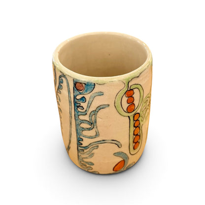 A handmade ceramic cup with a beige base, decorated with abstract hand-painted patterns in blue, green, and orange, shown on a white background.