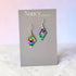 Colorful diamond-shaped earrings on a Nancy Jones card against a light background