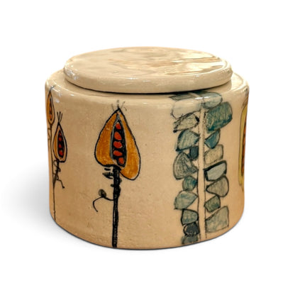 A round ceramic lidded container with a beige base and hand-painted botanical motifs in orange, green, and black, shown on a plain white background.