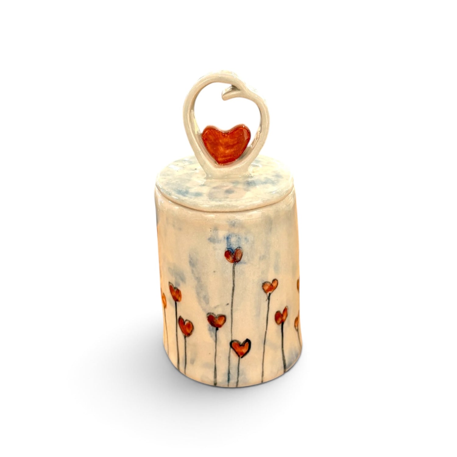 A small cylindrical ceramic keepsake box with a lid, decorated with red heart flowers on a cream-colored glaze. The lid features a heart-shaped loop handle holding a red heart.