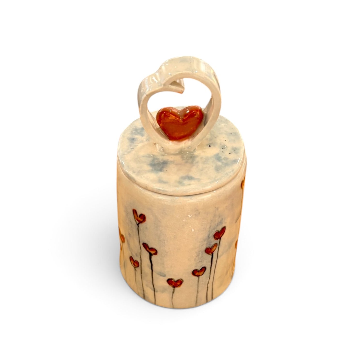 A small cylindrical ceramic keepsake box with a lid, decorated with red heart-shaped flowers on a beige background, featuring a heart-shaped ring topper with a red heart in the center, set against a plain white background.