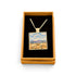 A square pendant necklace displayed inside an open tan gift box with a black velvet insert. The pendant has a gold-tone chain and border, with a colorful landscape painting in the center showing blue sky, white clouds, and a golden field.