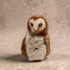A small felted wool owl figurine with brown and white feathers, standing against a textured beige background.