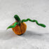 A small felted needle art pumpkin ornament in orange with a green stem and leaf, resting on a textured gray surface.