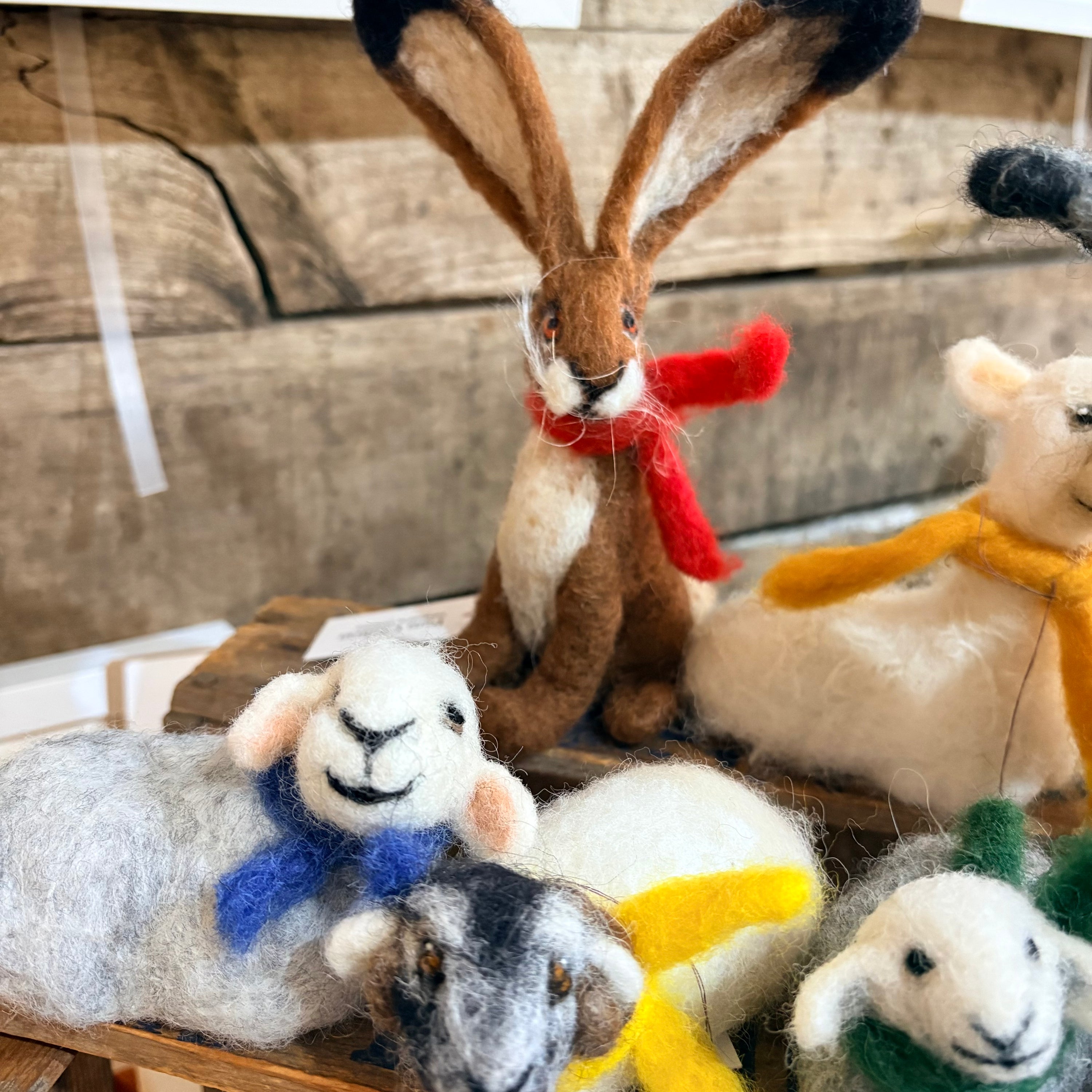 Collection of felted animal toys with scarves on a wooden surface