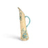 A tall, slender ceramic pitcher with a curved handle, featuring a cream-colored glaze decorated with turquoise blue floral and scroll patterns and small orange accents, set against a plain white background.