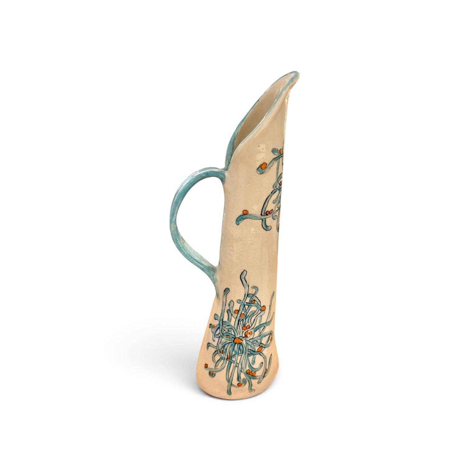 A tall, slender ceramic pitcher with a curved handle, featuring a beige body decorated with teal and orange abstract floral patterns, set against a plain white background.