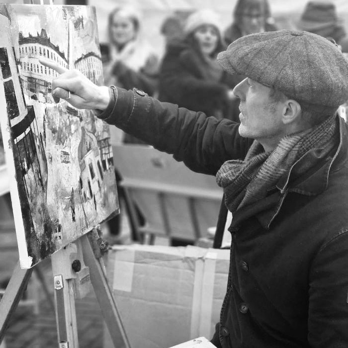 Richard Burel painting a cityscape on an easel with people in the background