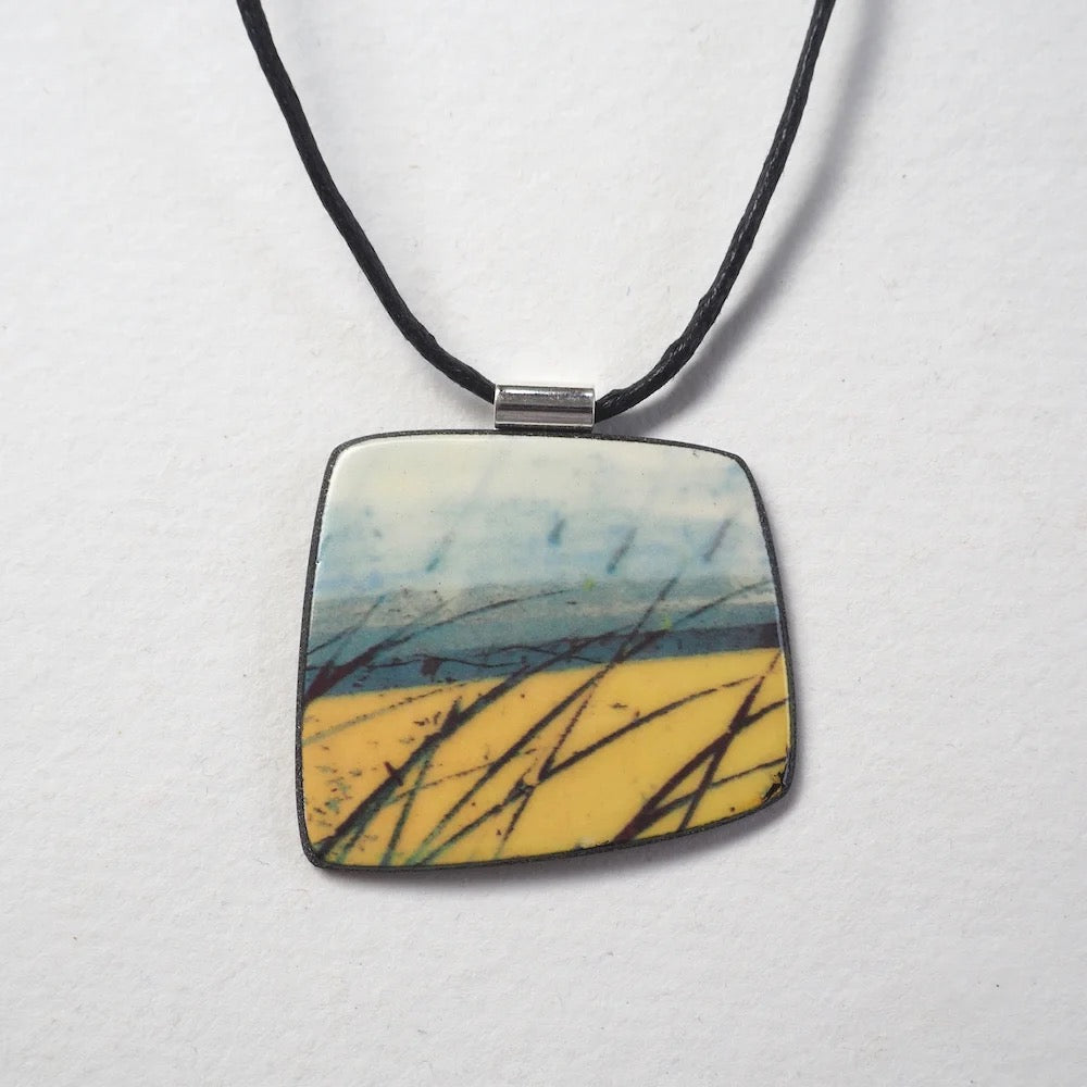 Square pendant with nature-themed design on a black cord against a white background