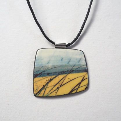 Square pendant with nature-themed design on a black cord against a white background