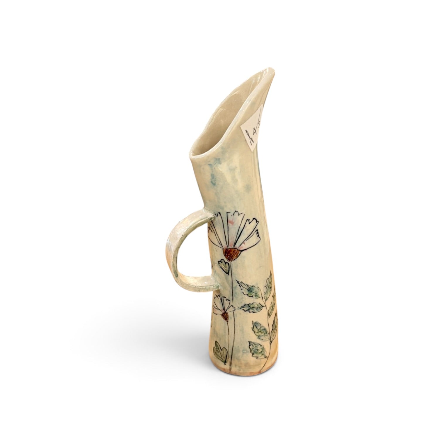 A handmade ceramic pitcher with a curved handle and a flared spout, decorated with hand-painted flowers and leaves on a cream-colored glaze.