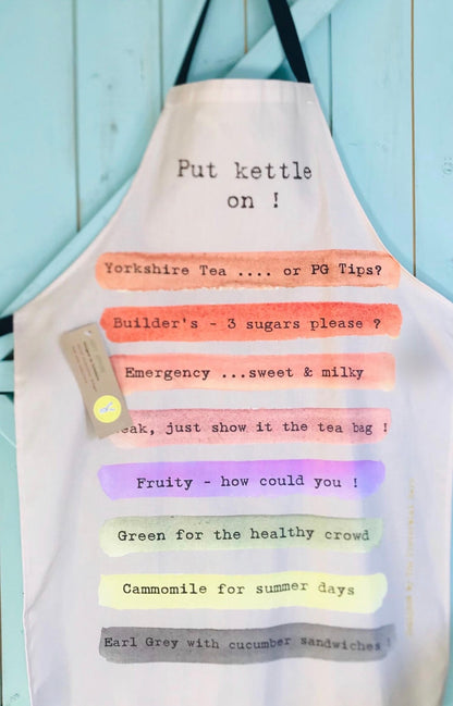 A white kitchen apron with black straps, featuring humorous printed text in black typewriter font over pastel watercolor stripes in orange, pink, green, purple, yellow, and gray. The text reads &