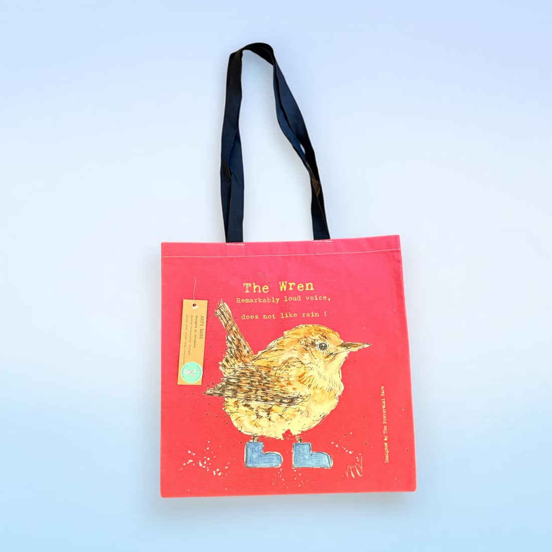 A red fabric tote bag with black handles, featuring a colorful illustration of a wren in yellow and blue boots, with the text &