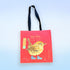 A red fabric tote bag with black handles, featuring a colorful illustration of a wren in yellow and blue boots, with the text &