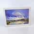 A square watercolor landscape art print in its original white paper border and plastic wrapping, showing a blue and purple sky over a reflective lake with trees and hills.