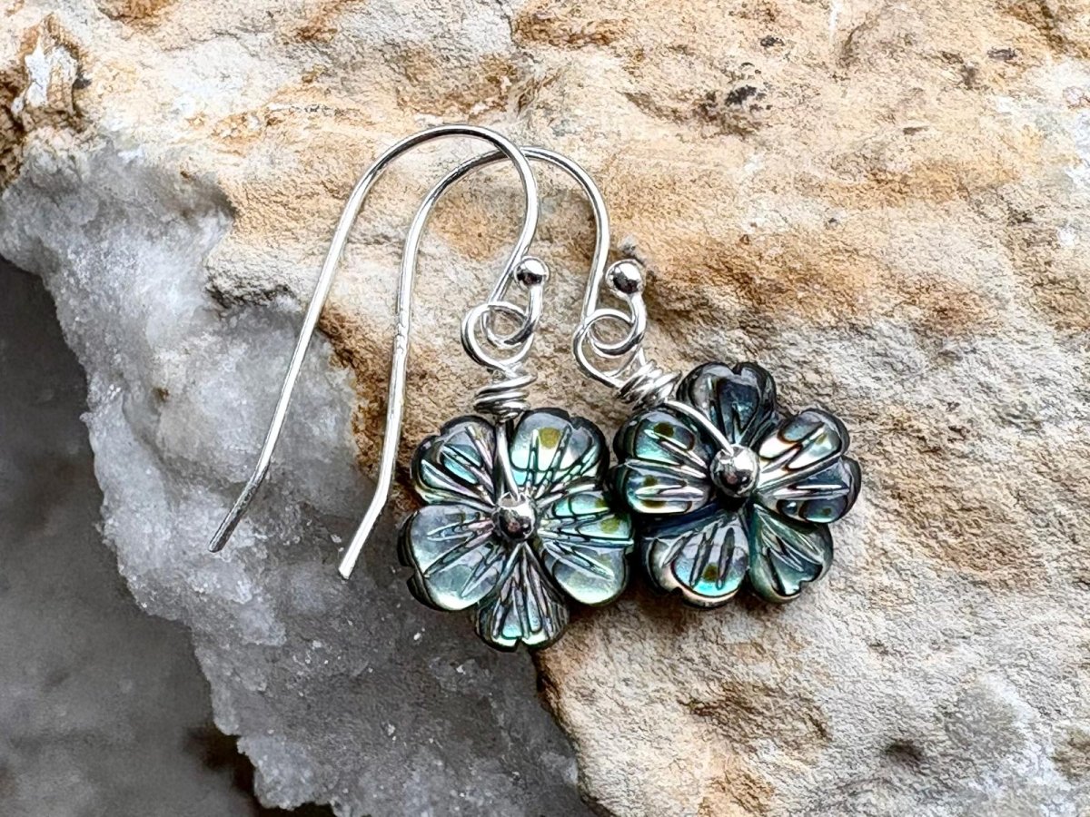 Floral silver earrings with green accents on a stone background