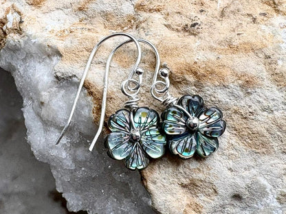 Floral silver earrings with green accents on a stone background