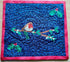 A square quilted fabric piece featuring a robin bird on a branch with mistletoe, set against a deep blue wavy background with small gold star-like details and a bright pink border.