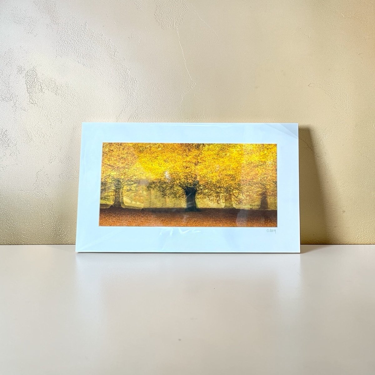 Mounted artwork of a yellow tree scene on a beige wall.