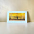 Mounted artwork of a yellow tree scene on a beige wall.