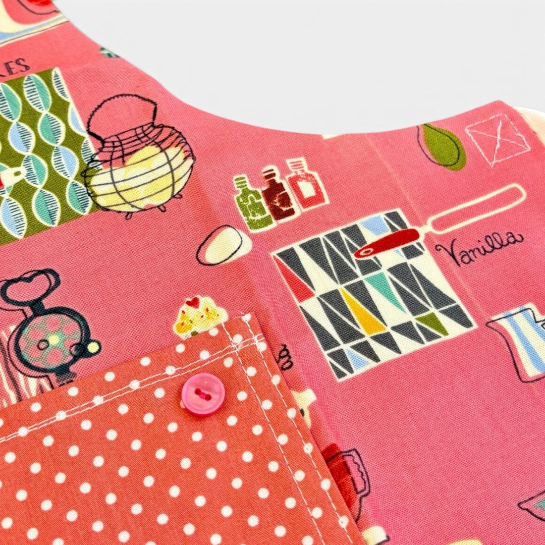 A close-up of a pink fabric garment or textile with a retro illustrated print, including a pocket with white polka dots and a pink button.