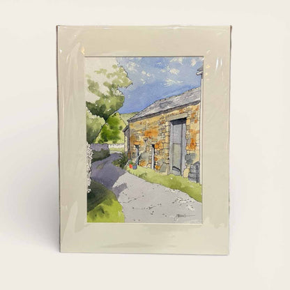 Framed watercolor painting of a stone building with a path and trees.