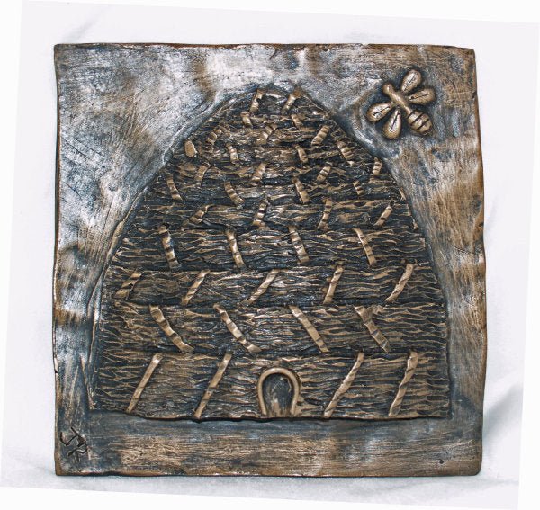 A square bronze relief sculpture depicting a beehive with a bee in the upper right corner, set against a plain white background.