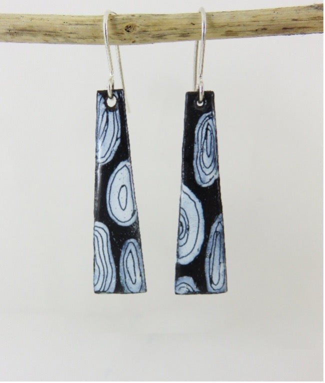 Black and white patterned earrings hanging from a branch on a light gray background