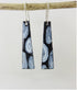 Black and white patterned earrings hanging from a branch on a light gray background