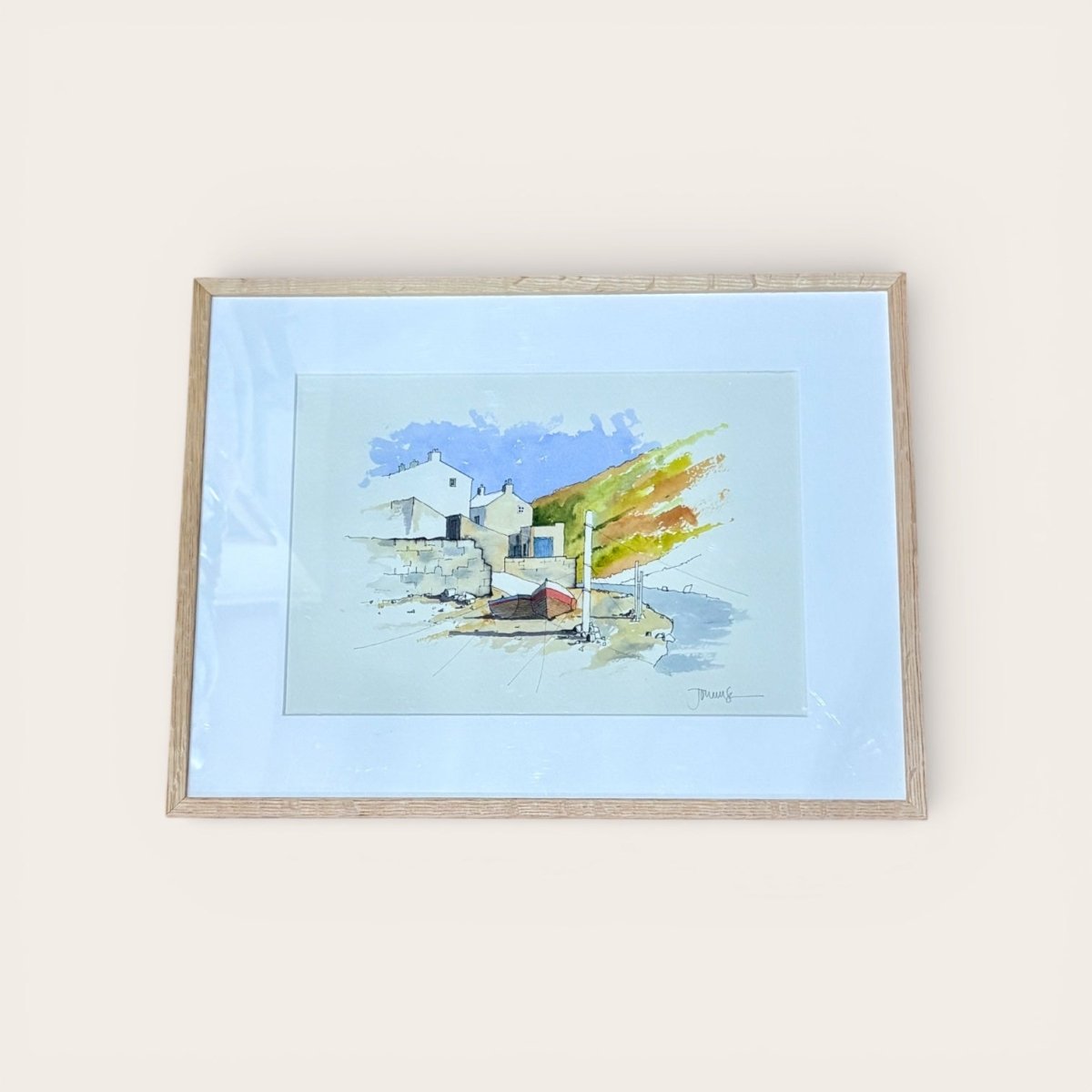 Framed watercolor painting of a coastal scene with houses and a blue sky.