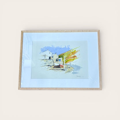 Framed watercolor painting of a coastal scene with houses and a blue sky.
