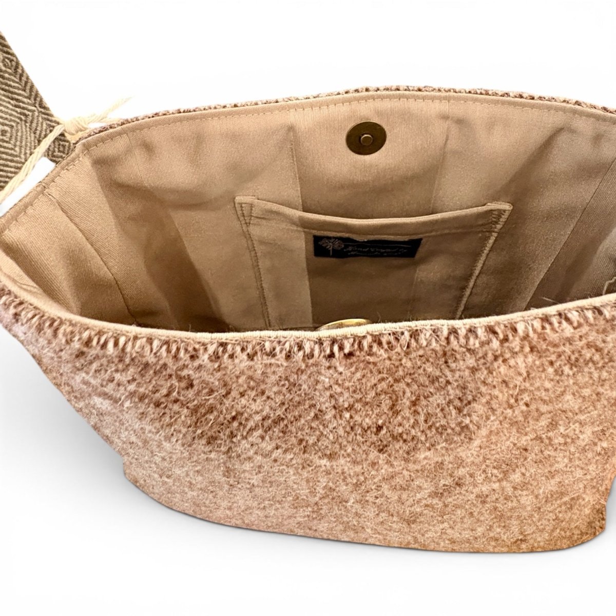 Close-up of the interior of a woven clutch or small handbag, showing a beige fabric lining, a front slip pocket, and a metal snap closure. The exterior fabric has a textured, heathered tan and brown pattern.