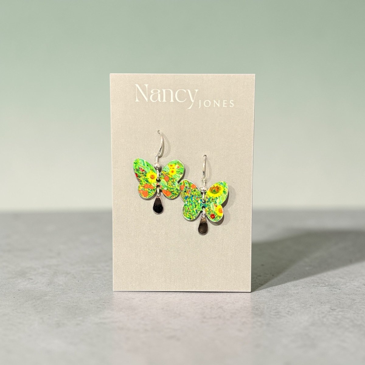 Butterfly-shaped earrings on a Nancy Jones card against a gray background