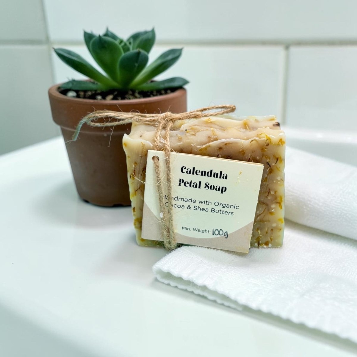 Calendula Petal Soap with a label on a white surface next to a potted plant.