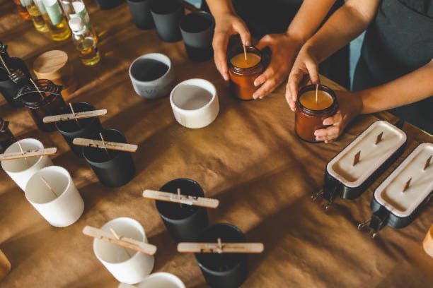 Hands arranging candles on a wooden table with various candle-making materials.