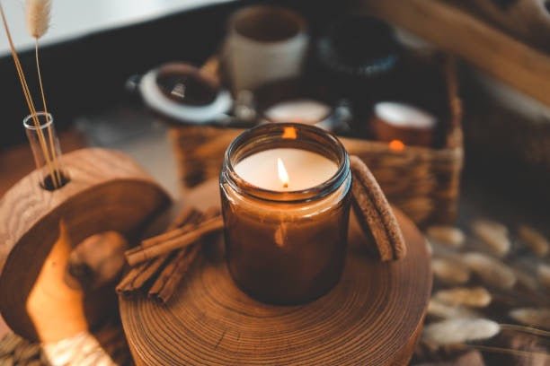 Candle in a glass jar on a wooden coaster with cinnamon sticks and a woven basket in the background.