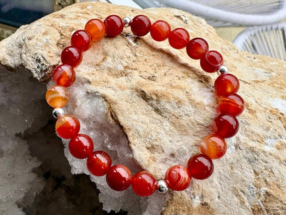 Red beaded bracelet with silver accents on a rock