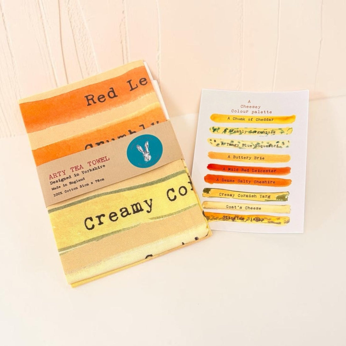 A set of pastel cotton tea towels in orange, yellow, and cream stripes, shown with their paper packaging labels on a light wood background.