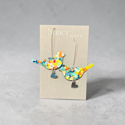 Colorful bird-shaped earrings on a Nancy Jones card against a gray background