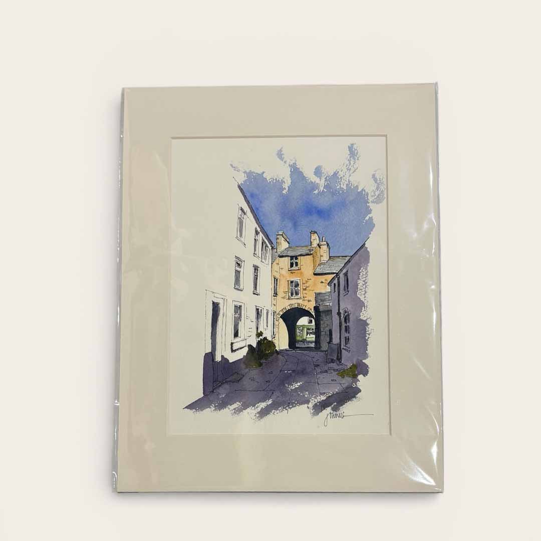 Framed artwork of a street scene with buildings and an archway on a light background
