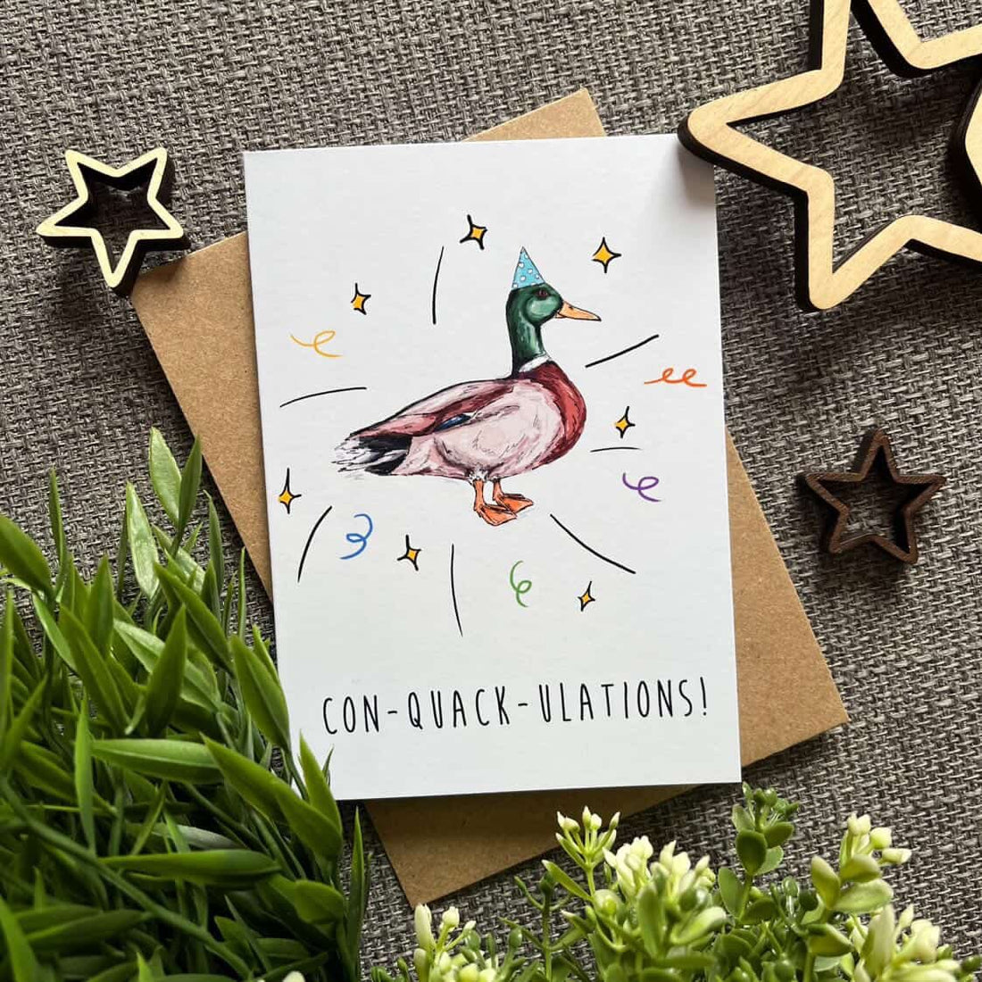 Greeting card with a duck illustration and text on a textured surface with decorative stars and plants.