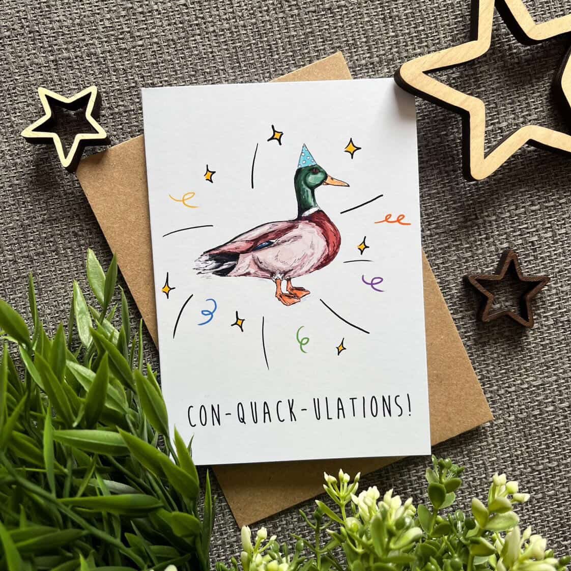 Greeting card with a duck illustration and text on a textured surface with decorative stars and plants.