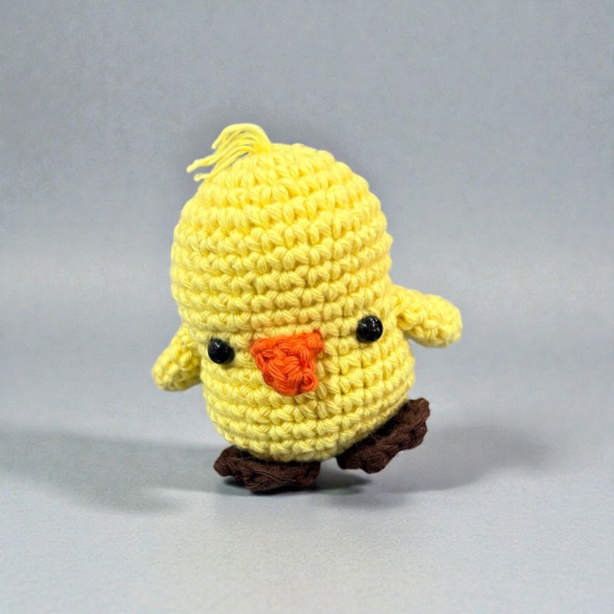 Crocheted yellow chick toy with orange beak on a gray background