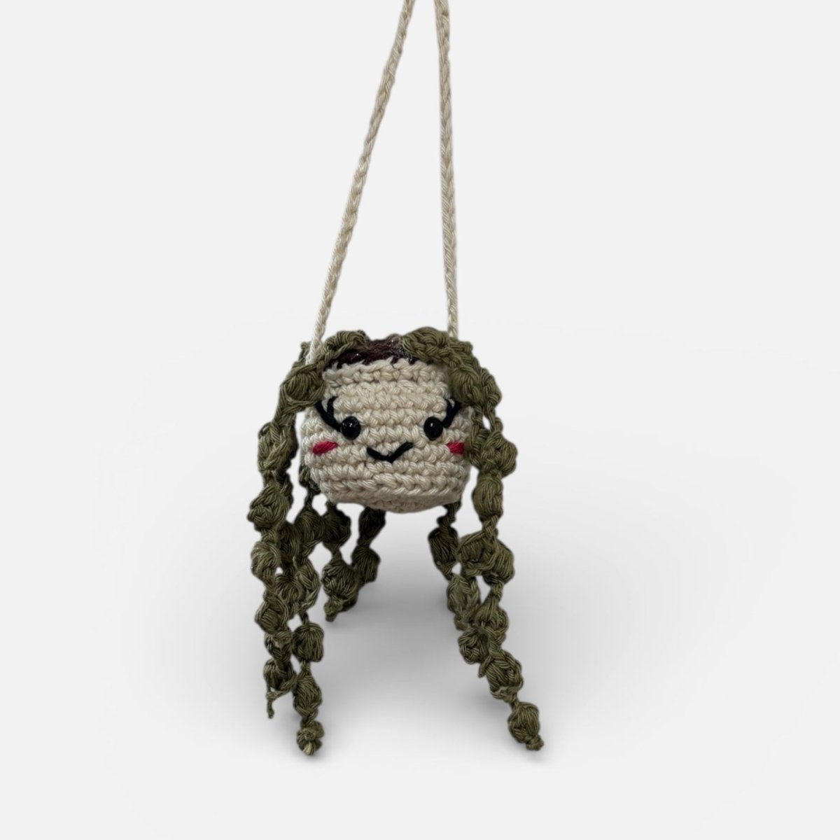 Crocheted character with braided hair hanging from a string on a white background