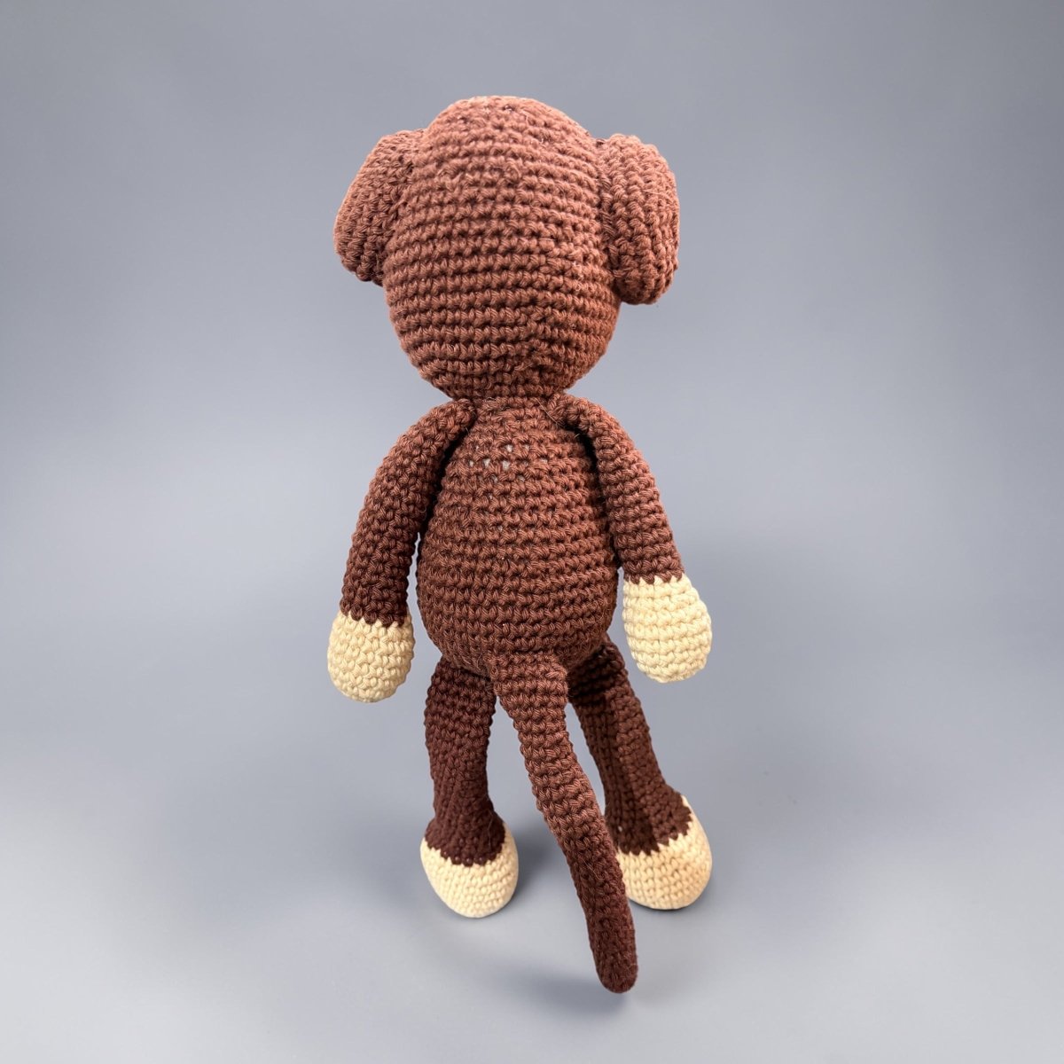 Brown crochet monkey toy on a gray background
