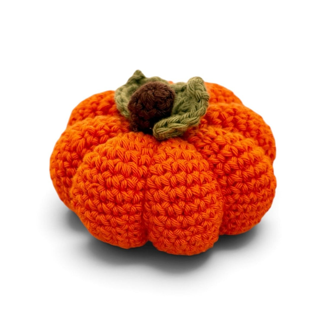 A crocheted pumpkin decoration in bright orange with a textured stem and leaves in brown and olive green, shown on a white background with a soft shadow.