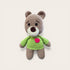 Crocheted teddy bear with a green sweater and pink heart on a light beige background